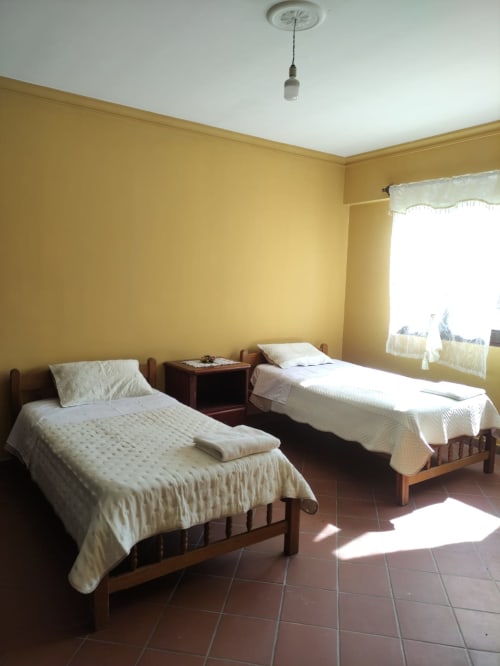 Dormitorio amarillo brillante con dos camas gemelas de madera y ropa de cama blanca en apartamento de Tarija con vista a la ciudad