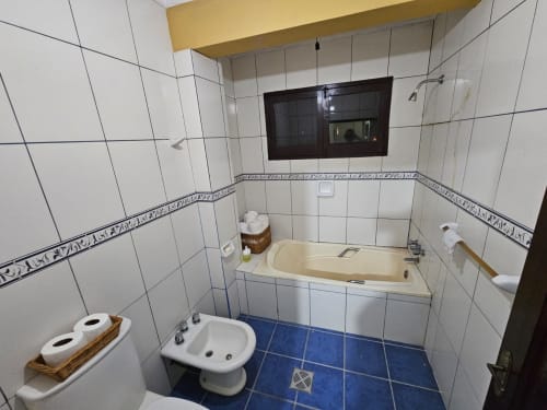 Baño moderno en apartamento de Tarija con azulejos blancos, piso azul, bidet, bañera y TV en la pared