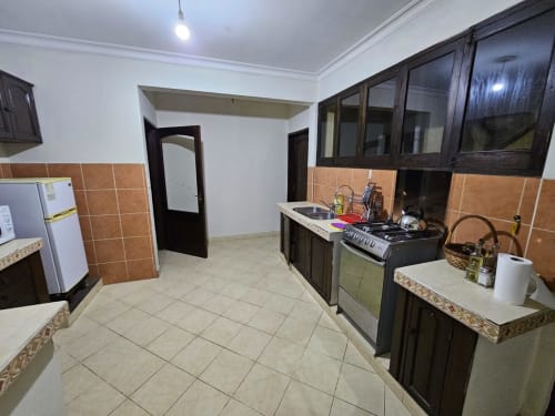 Cocina moderna en apartamento de Tarija con muebles oscuros, estufa, refrigerador y salpicadero de baldosas de barro