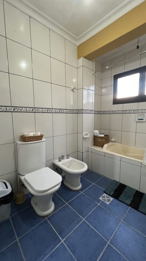 Baño moderno con azulejos blancos, piso azul, inodoro, bidé y bañera en apartamento de Tarija con vista a la ciudad