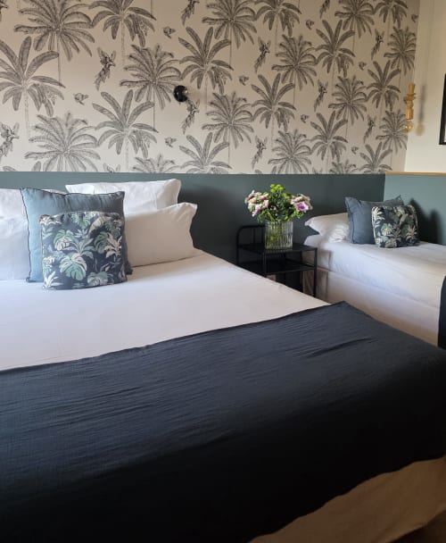 Chambre triple à l'Hôtel Les Lauriers à Saint-Tropez avec lits jumeaux, papier peint palmiers et vue sur jardin