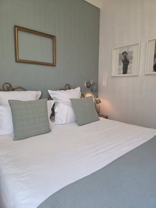 Chambre moderne à l'Hôtel Les Lauriers à Saint-Tropez avec literie blanche, coussins vert sage, tête de lit en bois et tableaux encadrés