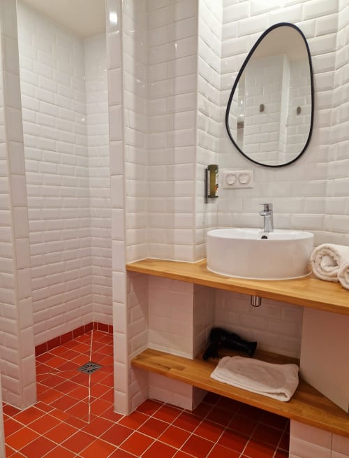 Salle de bains moderne de l'Hôtel Les Lauriers Saint-Tropez avec carrelage blanc, sol rouge, miroir rond, vasque et bois