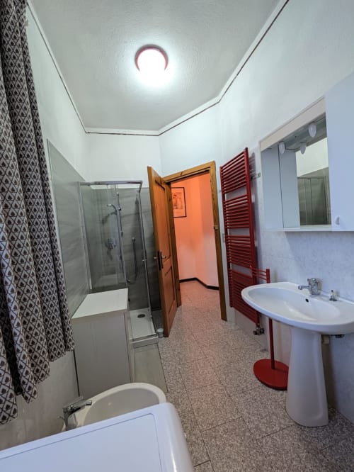 Salle de bains moderne de l'appartement QUADRIFOGLIO à Gio Appartamenti, Aymavilles, avec douche, lavabo, toilettes et sèche-serviettes chauffant rouge