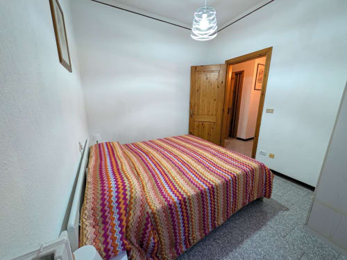 Lit aux rayures colorées dans la chambre spacieuse de Gio Appartamenti, Aymavilles, aux murs blancs et portes en bois