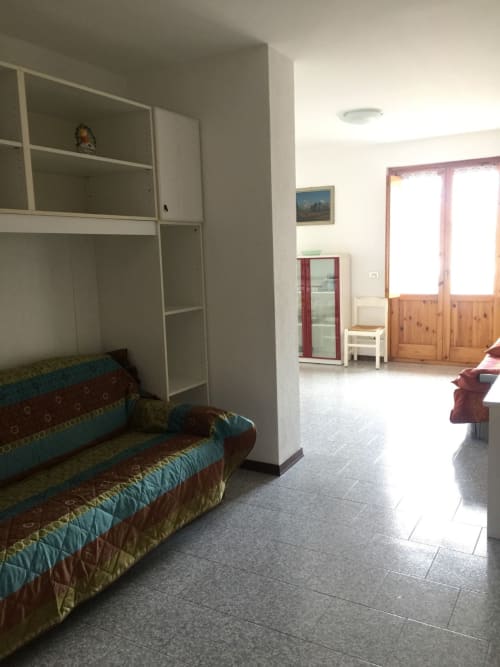 Spacieux séjour Gio Appartamenti à Aymavilles avec canapé, armoire intégrée et portes vitrées ouvertes sur la montagne