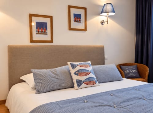 Lit double de la chambre d’hôtes Avel à Ty Coz Breizh, à Guidel en Bretagne Sud, avec coussin aux motifs de poissons, tête de lit beige et décoration bord de mer.