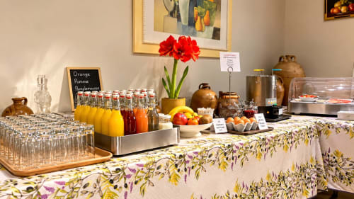 Hotel Les Oliviers breakfast buffet with juice selection, fresh fruits, pastries, and red flowers in Fayence