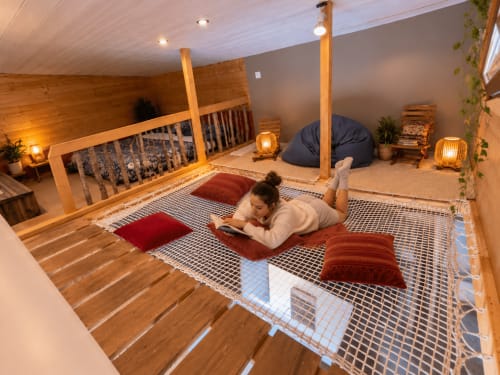 Femme lisant dans le grenier cosy d'une tiny house aux poutres bois, coussins et vue montagne au gîte de Chaparon, Lathuile