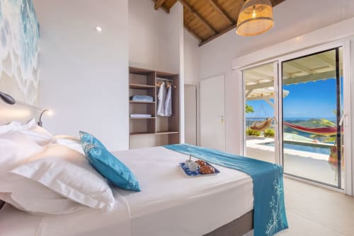 Chambre luxueuse avec vue mer aux Terrasses du Morne Gommier, lit blanc, accents bleus et terrasse océan