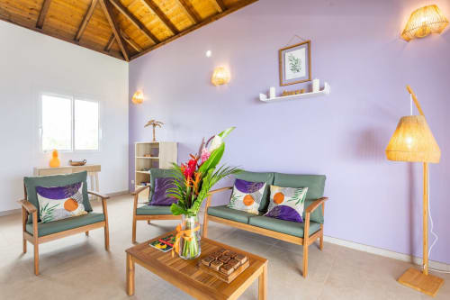 Salon de villa moderne aux murs lavande, mobilier vert, fleurs tropicales et meubles bois aux Terrasses du Morne