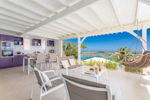 Villa de luxe aux Terrasses du Morne Gommier avec cuisine violette, poutres blanches, terrasse vue mer et chaise suspendue