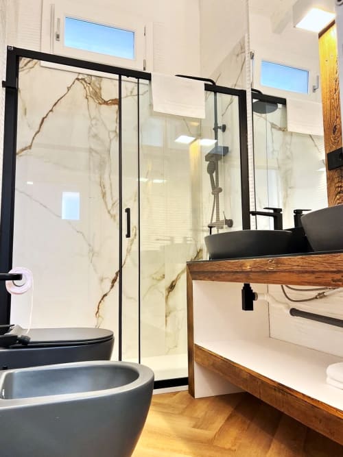 Bagno moderno presso La Sciumara Resort Palau con accessori neri, doccia in marmo, mobile lavabo in legno e illuminazione naturale