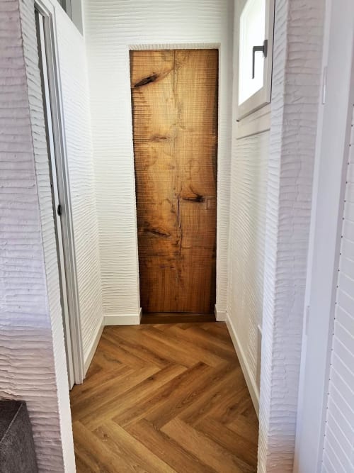Stretto corridoio con muri bianchi texturizzati, pavimento in legno a spina di pesce e rustica porta in legno al La Sciumara Resort Palau