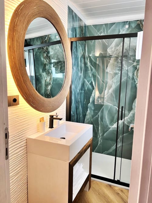 Bagno moderno della Resort La Sciumara a Palau con specchio circolare in legno, lavabo bianco e doccia rivestita in marmo verde