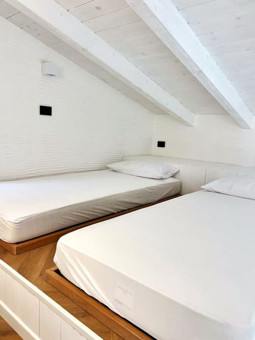 Accogliente camera in soffitta con due letti, muri in mattoni bianchi, travi a vista e cornici in legno al La Sciumara Resort Palau
