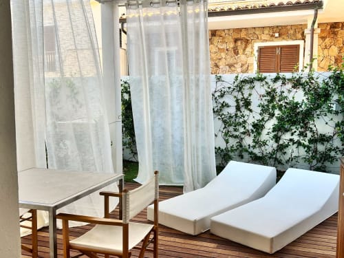 Veranda rilassante al La Sciumara Resort Palau con lettini bianchi, tende trasparenti e muri del giardino ricoperti di edera a Palau