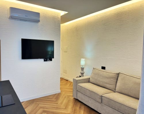 Moderno soggiorno al La Sciumara Resort Palau con TV a parete, divano beige, pareti bianche texture e pavimento in legno