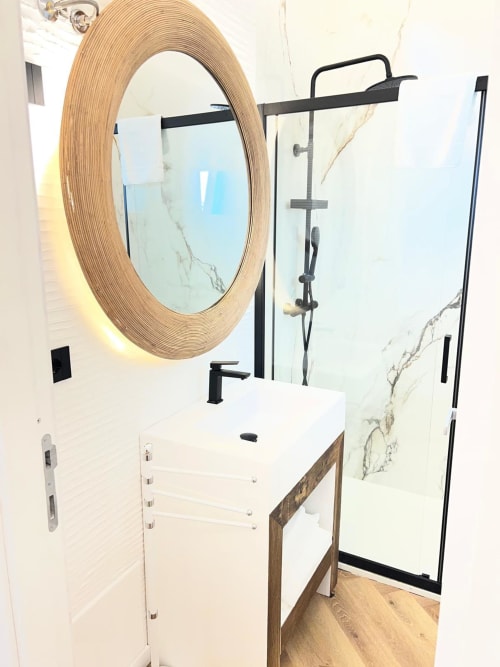 Bagno moderno al La Sciumara Resort Palau con specchio rotondo cornice in legno, lavabo bianco, rubinetteria nera e doccia in marmo