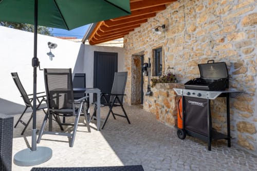 Pátio exterior de Recantos D'Almerinda com mesa de jantar, guarda-sol, grill e paredes de pedra em Pombal, Portugal