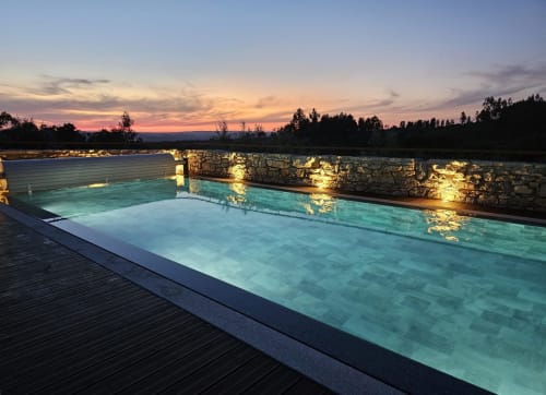 Piscina de borda infinita do Recantos D'Almerinda em Pombal, Portugal, iluminada ao pôr do sol com floresta ao fundo