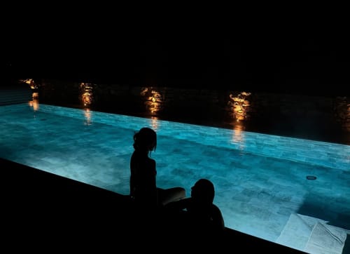 Dois hóspedes aproveitam a piscina azul iluminada do Recantos D'Almerinda em Pombal, Portugal, à noite.