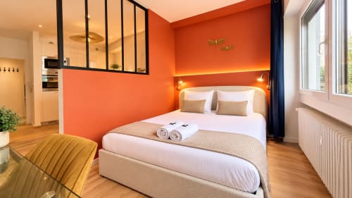 Chambre moderne à Mattbnb Luxembourg Limpertberg avec murs orange vif, lit blanc, parquet et vue sur la ville