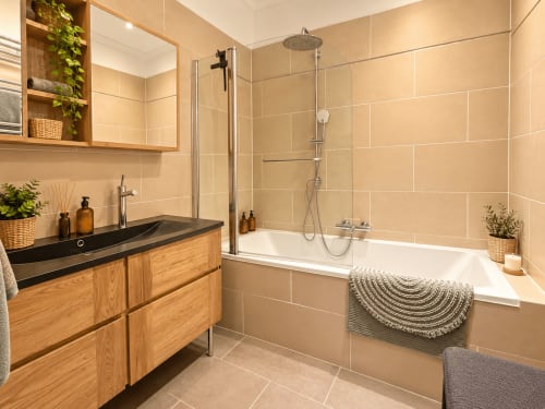 Salle de bain moderne de Mattbnb Metz avec vasque en bois, lavabo noir, douche italienne, baignoire et carrelage beige chaleureux.