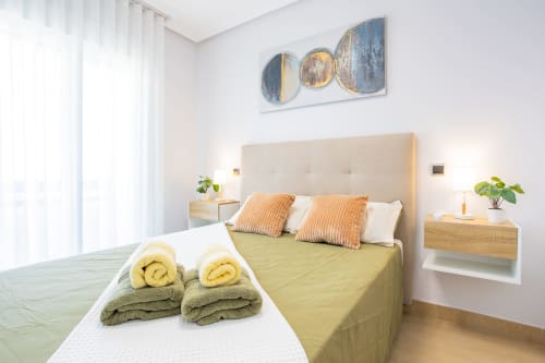 Dormitorio moderno en Haus Holiday Homes en San Pedro del Pinatar con cabecero crema, ropa de cama amarilla, toallas enrolladas y