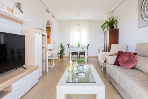 Moderno salón en Haus Holiday Homes, San Pedro del Pinatar, con sofá, televisión, comedor y plantas decorativas