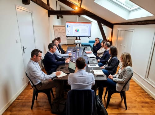 Réunion d'affaires dans la salle de conférences du loft moderne de Vindihouses Epinac avec l'équipe autour de la table consultant une présentation