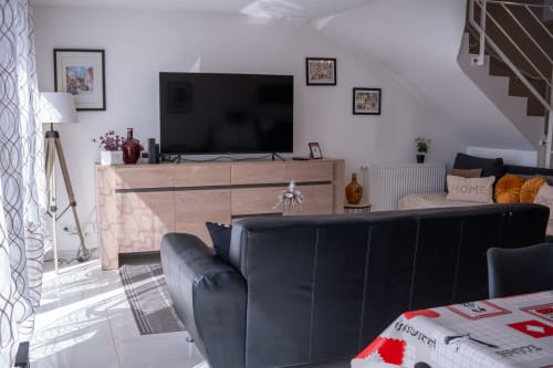 Sala de estar moderna en la casa rural La Vénitienne, Colmar, con sofá de cuero negro, mueble TV de madera y escalera
