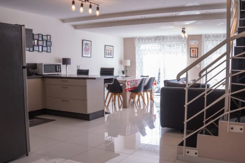 Sala de estar moderna y abierta en Les Ambrades Colmar con cocina, mesa de comedor, muebles negros y escalera