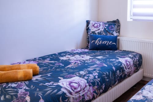 Acogedora habitación en Les Ambrades, Colmar con ropa de cama floral azul marino, rosas púrpura, almohada 'home' y toallas naranjas enrolladas