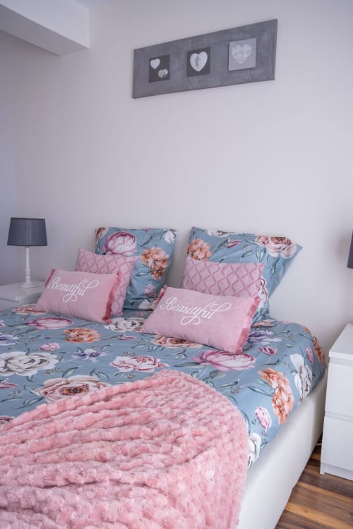 Dormitorio de la casa rural Les Ambrades en Colmar con ropa de cama floral, almohadas rosas y decoración mural de corazones