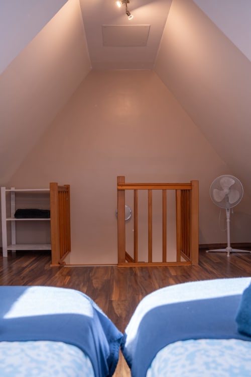 Acogedora habitación abuhardillada en la casa rural Les Ambrades de Colmar con cuna de madera, estanterías blancas y ventilador de pie