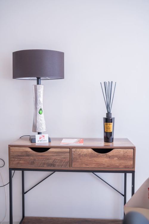 Escritorio moderno con lámpara texturizada, difusor de varitas y revista en la habitación de la Casa Les Ambrades, Colmar