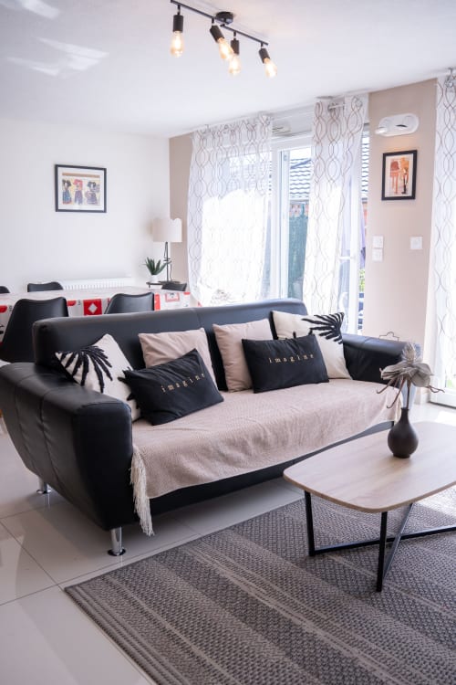 Sala moderna con sofá negro, manta beige, cortinas estampadas y mesa de café de madera en la casa rural La Vénitienne