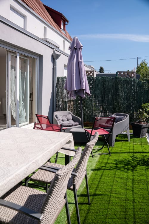 Terraza soleada de la casa rural La Vénitienne en Colmar con tumbonas, sombrilla morada y jardín cuidado rodeado de vegetación
