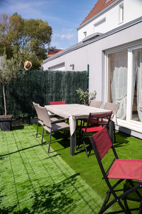 Terraza exterior de la casita La Vénitienne en Colmar con mesa de comedor, sillas rojas y jardín bien cuidado