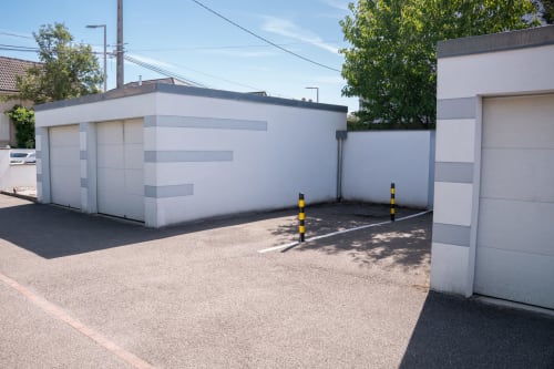 Modernos edificios de garaje blancos en Les Ambrades de Colmar con acceso pavimentado y bolardos amarillos