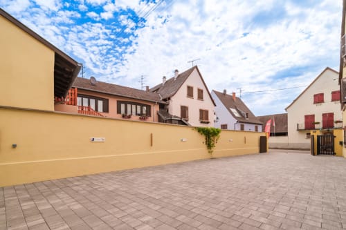 Encantador patio de Sigolsheim con pared amarilla, edificios alsacianos tradicionales y cielo azul en el hotel Les Ambrades