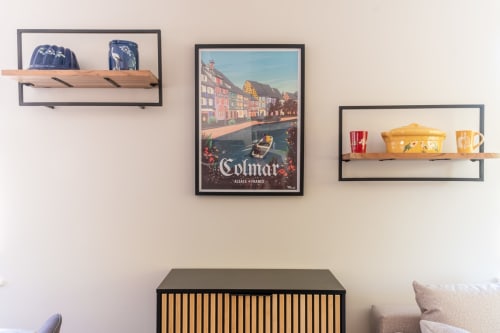 Decoración de pared de habitación de hotel en Kaysersberg con estantes flotantes, cerámica azul, alfarería amarilla y póster de viaje de Colmar