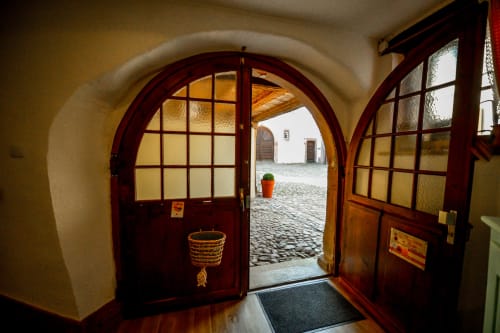 Puerta arqueada de madera que se abre a un patio empedrado en la casa rural Les Ambrades en Riquewihr