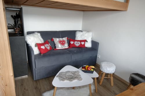 Sala de estar acogedora en la casa rural Les Ambrades con sofá gris, almohadas rojas con corazones, detalles de pelaje blanco y mesita de café en Gérardmer