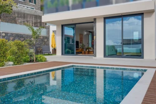 Vila moderna branca com piscina reluzente, deck de madeira e portas de vidro nas Residências BHF, Arco da Calheta, Portugal