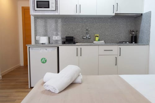Piccola cucina moderna con armadi bianchi, piano di lavoro grigio, microonde e frigorifero ad alta efficienza energetica ad Apartamentos El Sol