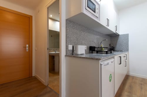Cucinetta moderna negli Apartamentos El Sol II Tossa de Mar con top in granito, elettrodomestici bianchi e porta d'ingresso in legno