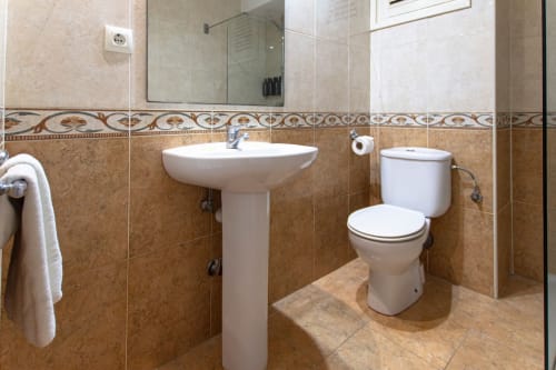 Bagno moderno negli Apartamentos El Sol II, Tossa de Mar con lavabo a colonna, toilet e pareti piastrellate con bordo decorativo