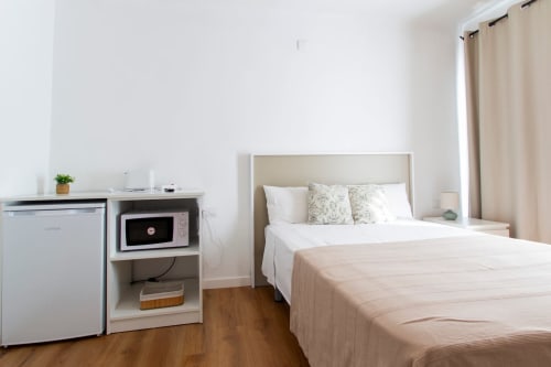 Dormitorio moderno en Tossa de Mar con cama de matrimonio, cocineta, microondas y cortinas beige